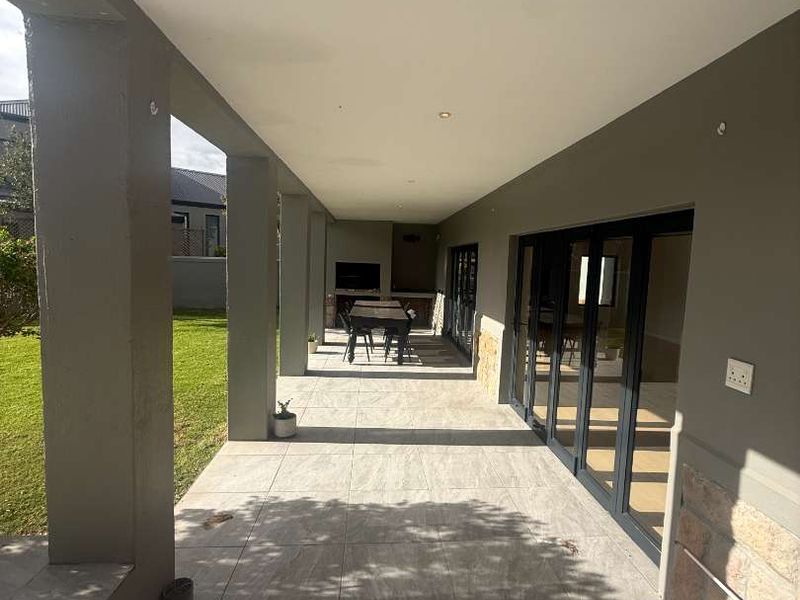 A spacious covered patio featuring large format floor tiles, recessed lighting, and a built-in braai, seamlessly connecting to the interior through modern stacking doors.