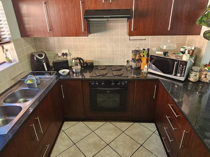 Functional U-shaped kitchen featuring dark wood cabinetry, granite countertops, a double stainless steel sink, and built-in electric cooking appliances.
