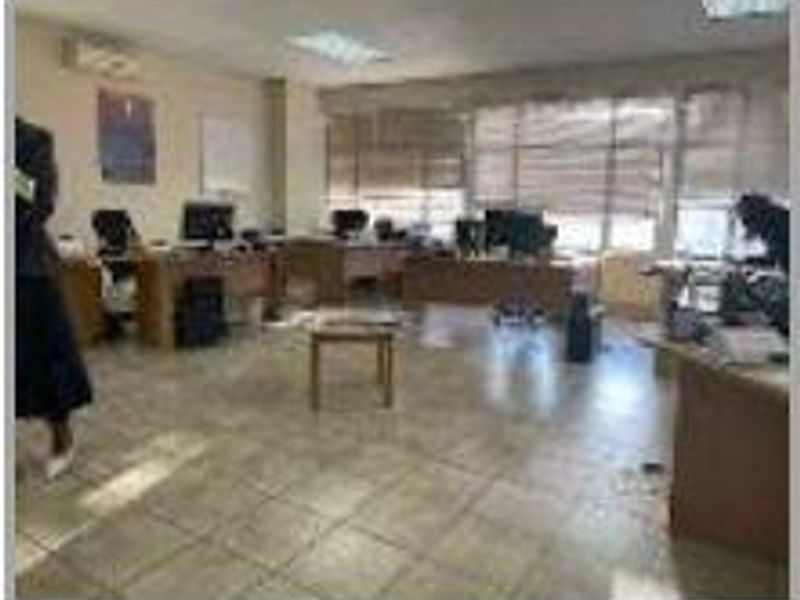 A functional office space featuring tiled flooring, recessed lighting, and large windows with blinds, providing a practical work environment.