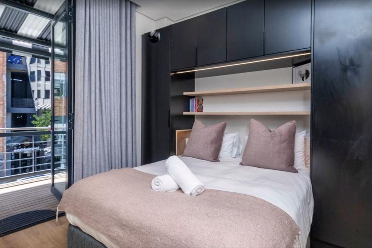 Modern bedroom featuring built-in floor-to-ceiling cabinetry, integrated shelving, and direct access to a private balcony through glass doors.