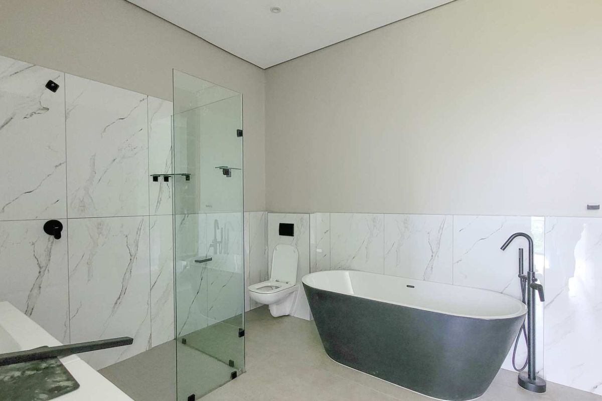 Modern bathroom featuring a sleek freestanding bathtub, a spacious walk-in shower with glass enclosure, and contemporary black matte fixtures against marble-look wall tiles.