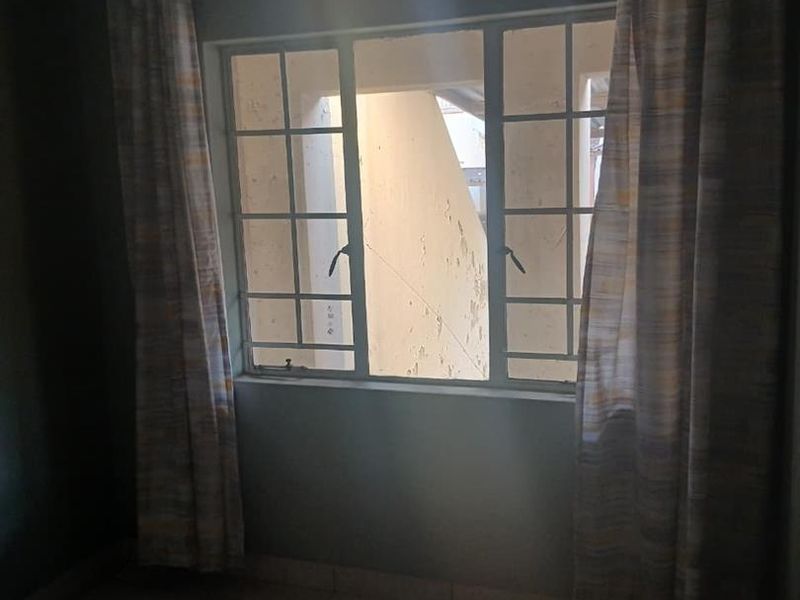 An empty bedroom featuring tiled flooring and a window with security bars, offering a view of the exterior building facade.