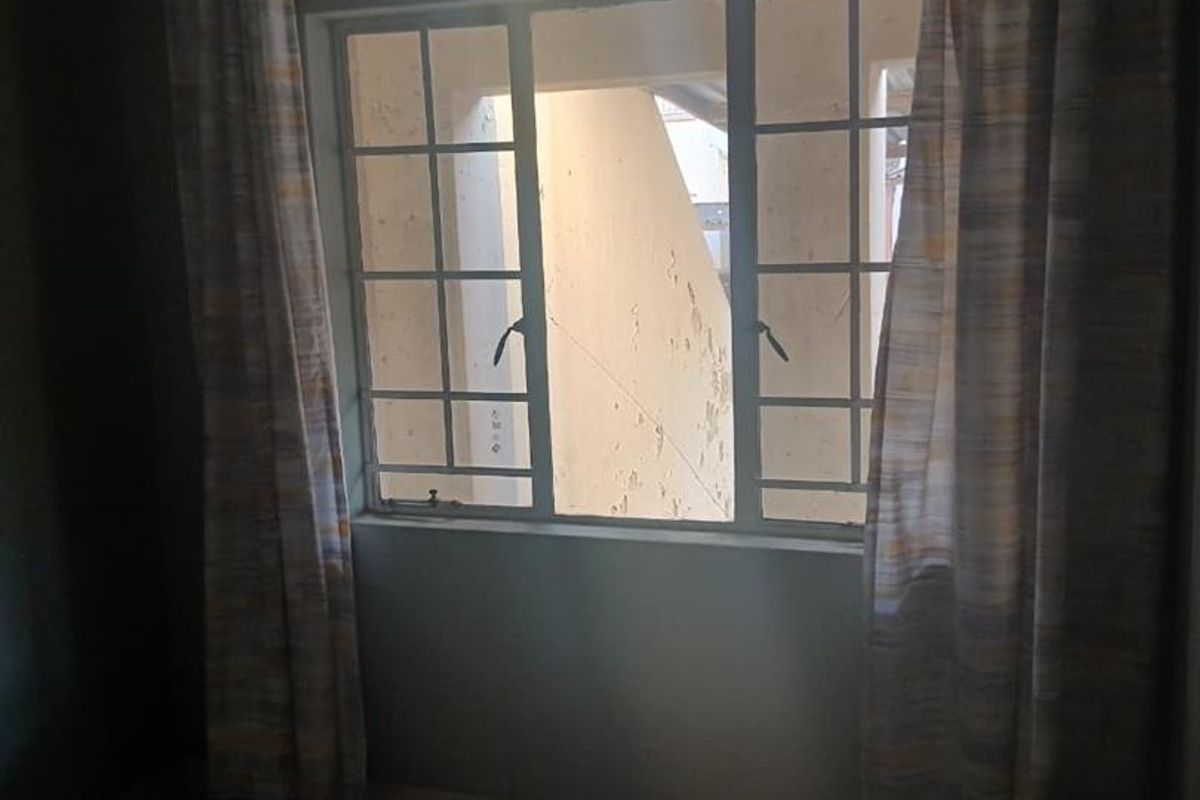 An empty bedroom featuring tiled flooring and a window with security bars, offering a view of the exterior building facade.