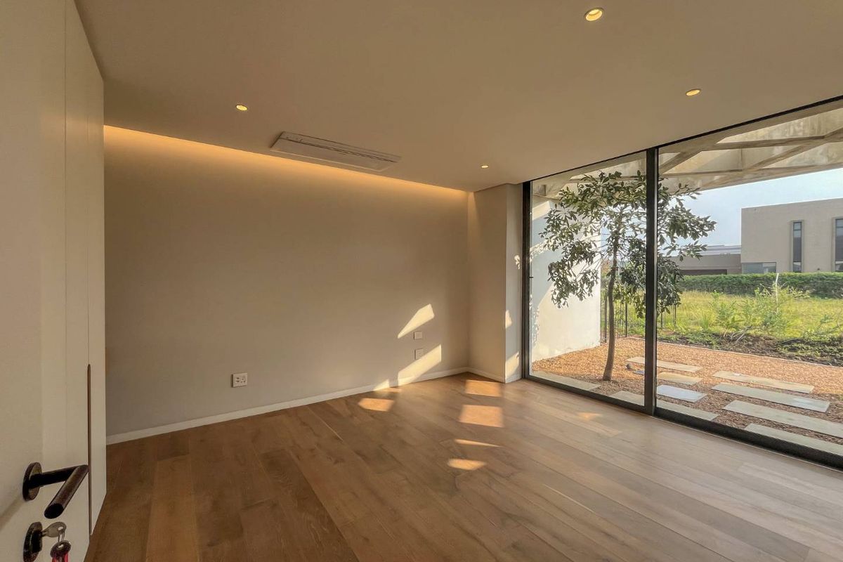 A bright, modern bedroom featuring high-quality timber flooring, recessed ceiling lighting, integrated air conditioning, and floor-to-ceiling glass doors opening to a private garden.