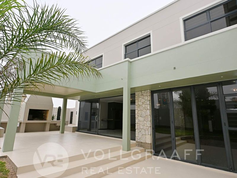 A modern covered patio featuring a built-in braai, stone accents, and large sliding glass doors providing seamless indoor-outdoor flow.