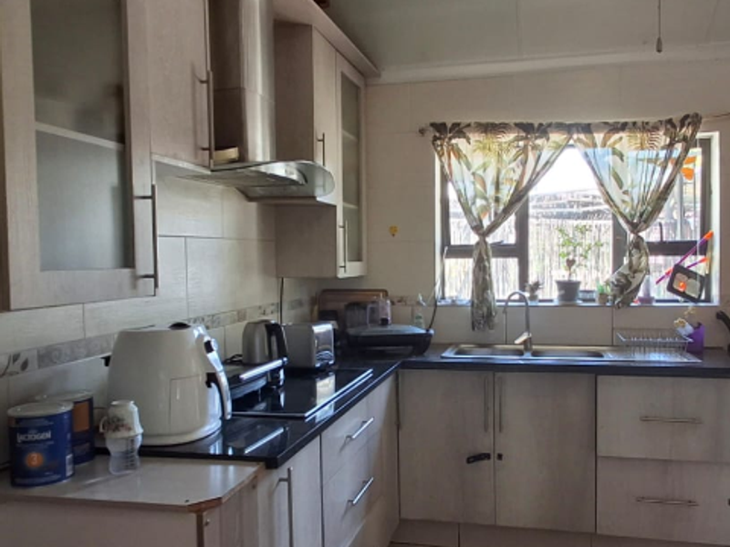 A functional kitchen featuring light-toned built-in cabinetry, a tiled backsplash, a double sink, and a built-in hob with an extractor fan.