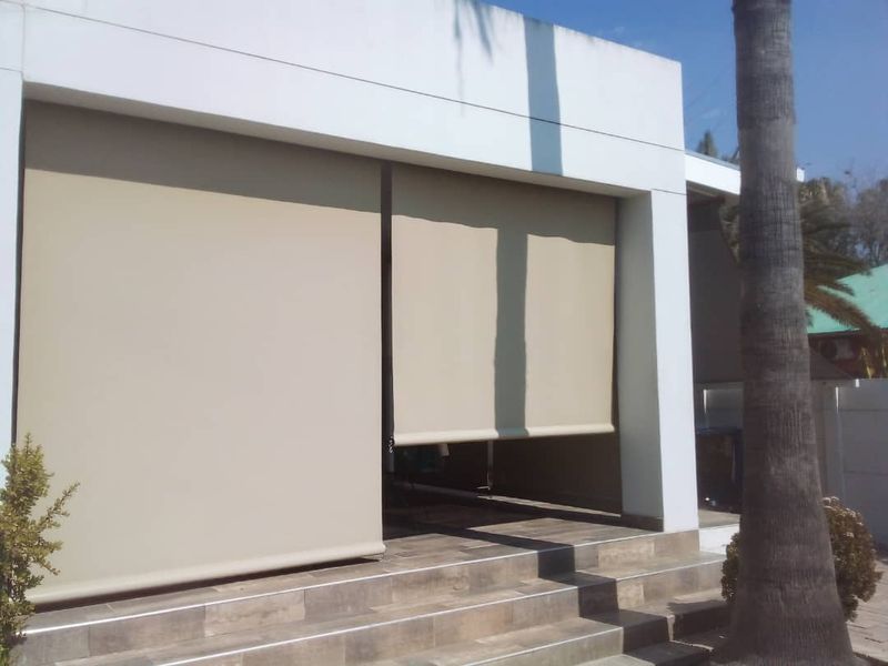 A covered patio area featuring tiled flooring, concrete steps, and retractable outdoor blinds for shade and privacy.