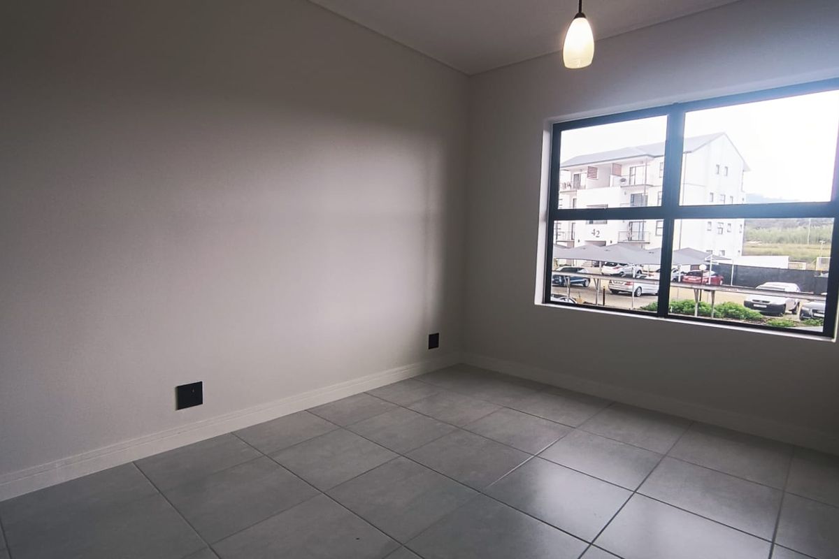 A bright, empty bedroom featuring neutral tiled flooring, large window with natural light, and a modern pendant light fixture.