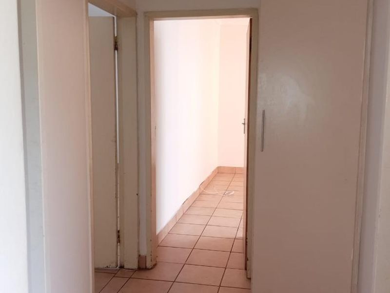 A vacant hallway featuring tiled flooring and a built-in cupboard, providing access to adjacent rooms within the apartment.