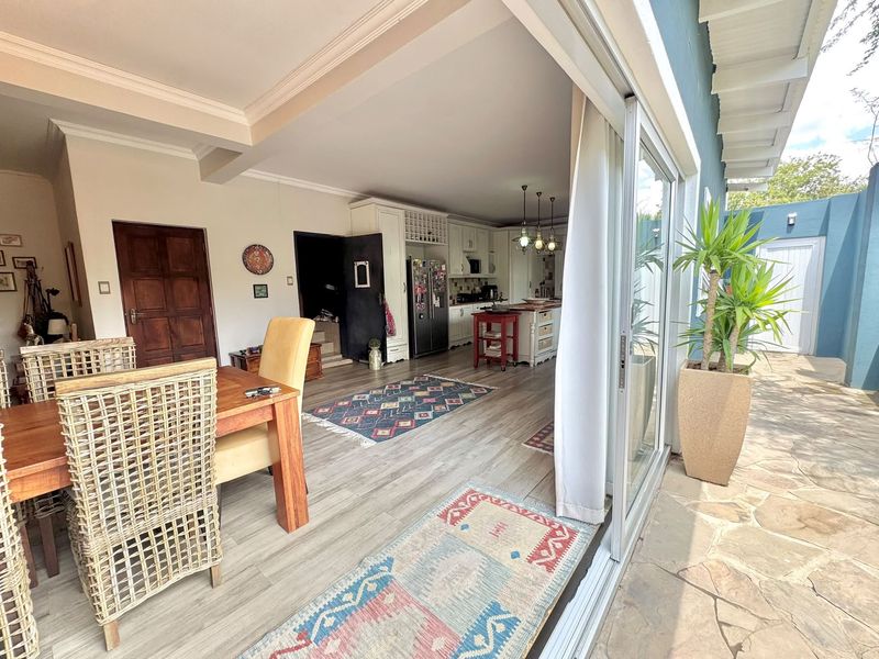 Open plan living and dining area flowing seamlessly onto a stone-paved patio through large sliding glass doors, featuring a well-appointed kitchen with island.