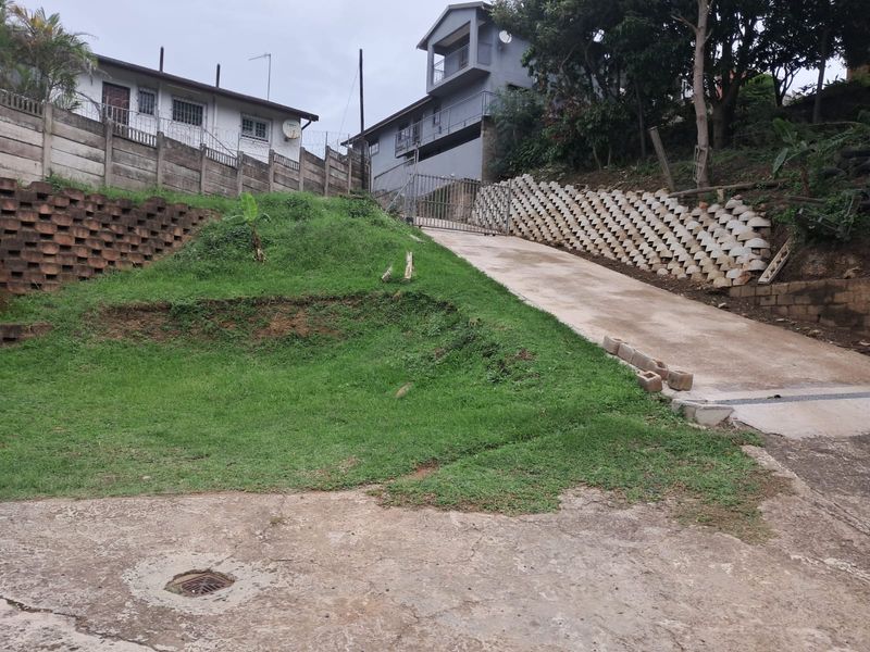Sloped concrete driveway leading to a gated entrance, featuring tiered retaining walls and an embankment area.