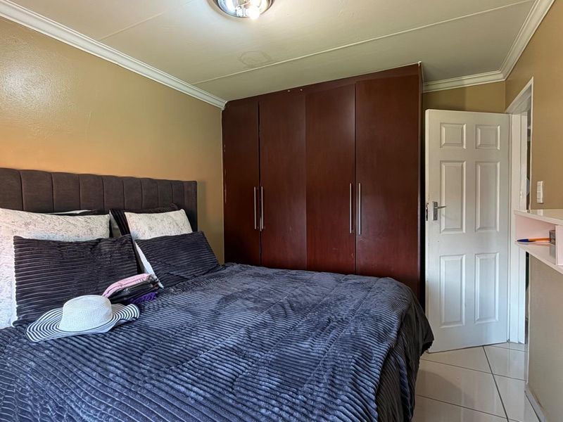 A bedroom featuring tiled flooring, a built-in dark wood wardrobe, and neutral wall tones.