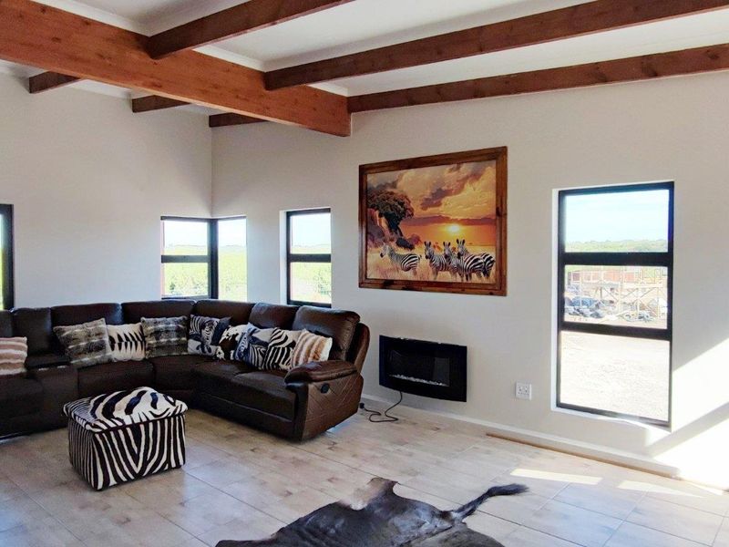 Spacious living area featuring exposed timber ceiling beams, tiled flooring, and a wall-mounted electric fireplace, with large windows offering expansive rural views.