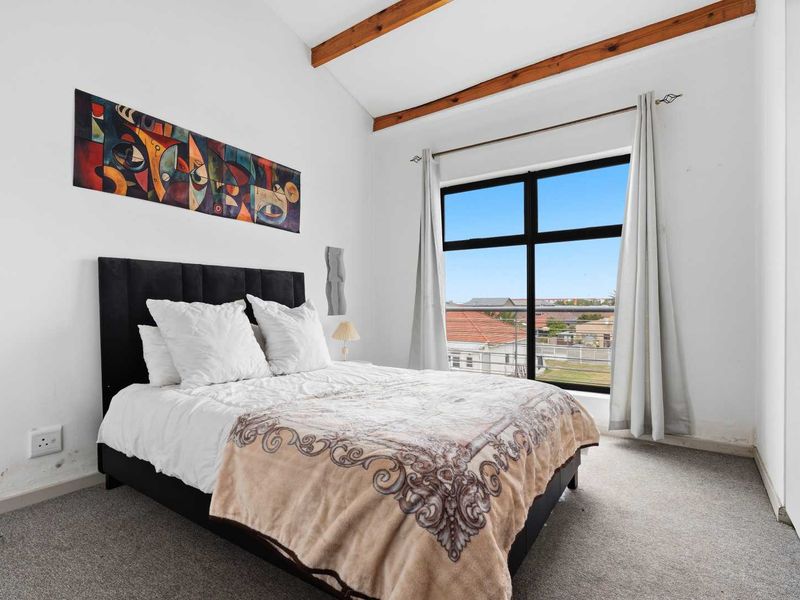 A bright bedroom featuring exposed timber ceiling beams, a built-in wardrobe, and a large window providing natural light and neighborhood views.