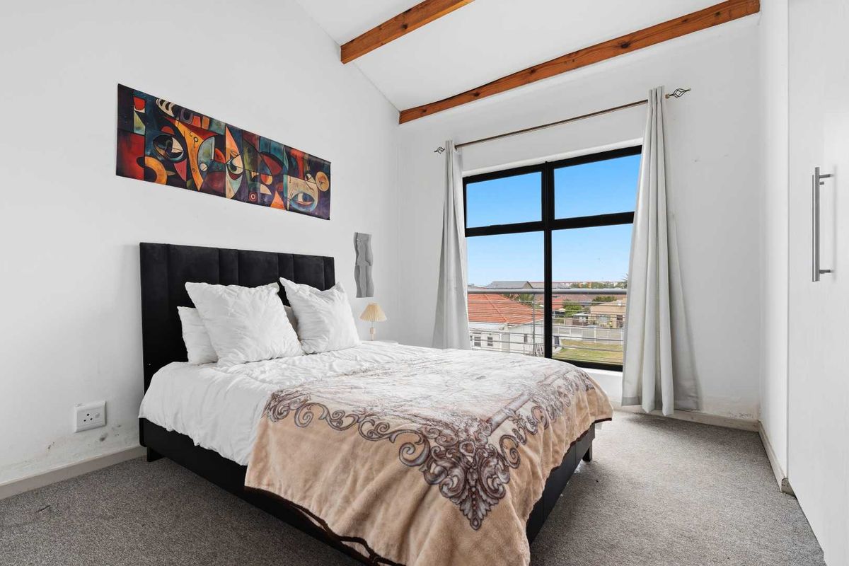 A bright bedroom featuring exposed timber ceiling beams, a built-in wardrobe, and a large window providing natural light and neighborhood views.