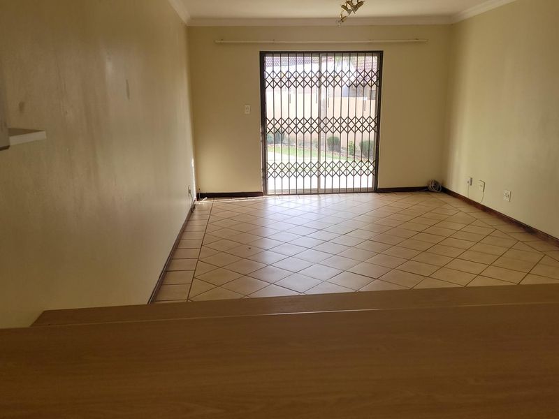 An empty living room featuring tiled flooring and a sliding door with a security gate, providing direct access to the exterior.