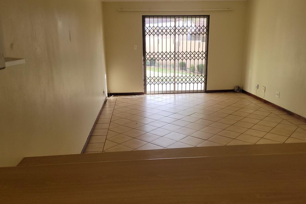 An empty living room featuring tiled flooring and a sliding door with a security gate, providing direct access to the exterior.