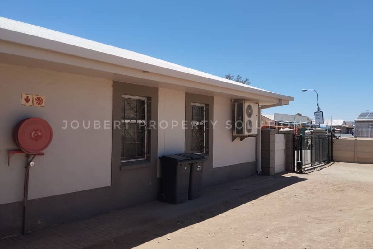 Exterior view of the business premises featuring a side facade, security window bars, wall-mounted fire hose reel, and external air conditioning unit.