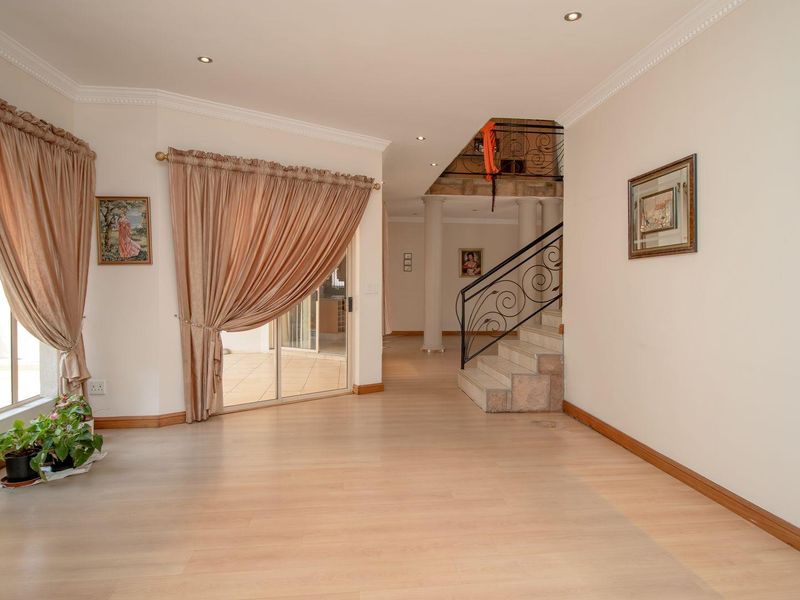 Spacious living area featuring light laminate flooring, crown molding, recessed lighting, and a decorative wrought iron staircase leading to the upper level.