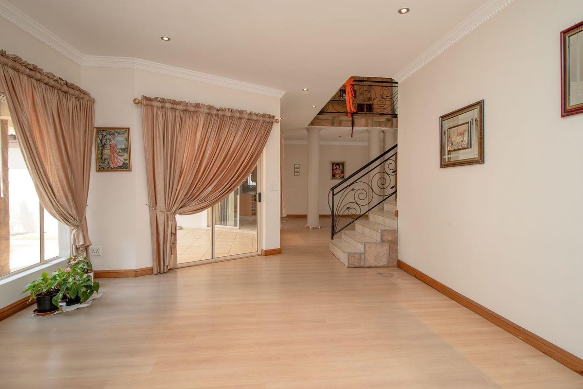 Spacious living area featuring light laminate flooring, crown molding, recessed lighting, and a decorative wrought iron staircase leading to the upper level.