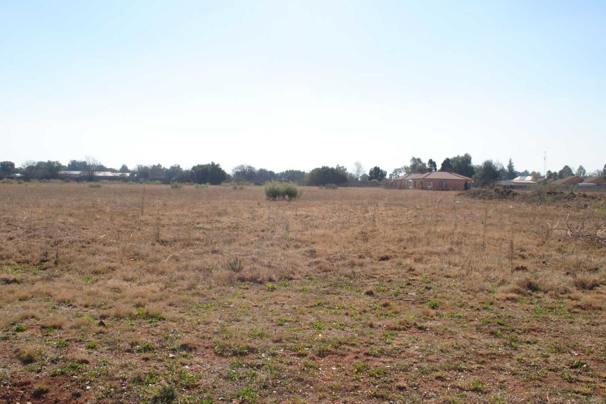 A wide-angle view of a vacant residential plot featuring natural dry grass and open space, suitable for future development.