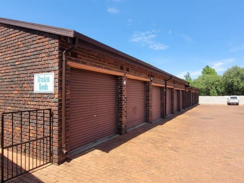 A row of brick-built garages with roller shutter doors situated in a paved complex courtyard.
