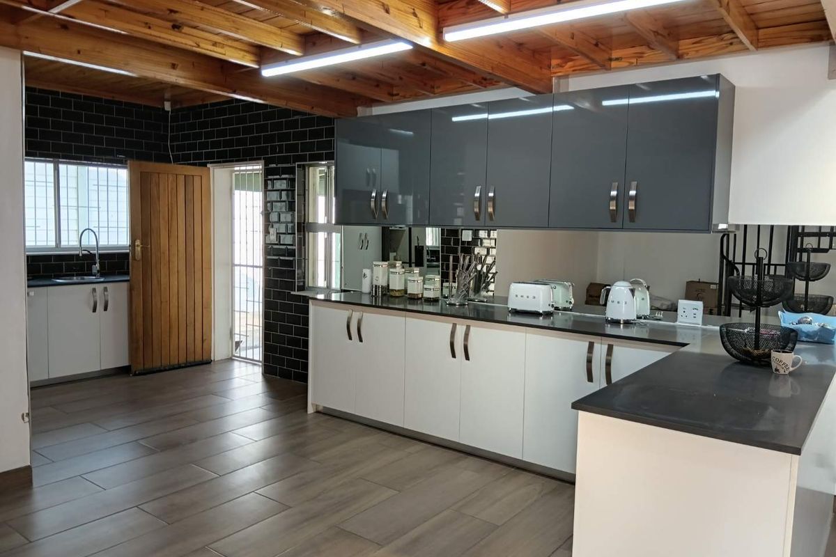 Modern kitchen featuring contrasting grey and white cabinetry, dark stone countertops, black subway tile backsplash, and a distinctive exposed timber beam ceiling.