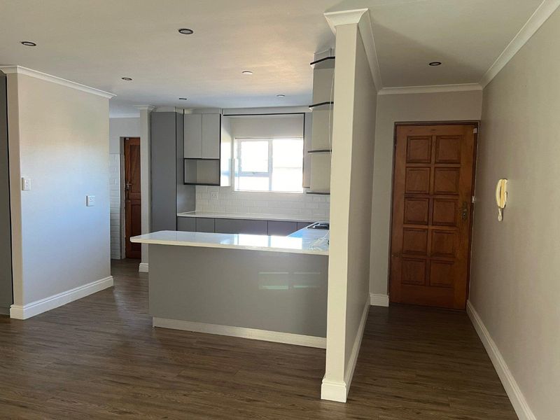An open-plan living and kitchen area featuring modern grey cabinetry, stone countertops, subway tile backsplash, and wood-look laminate flooring.