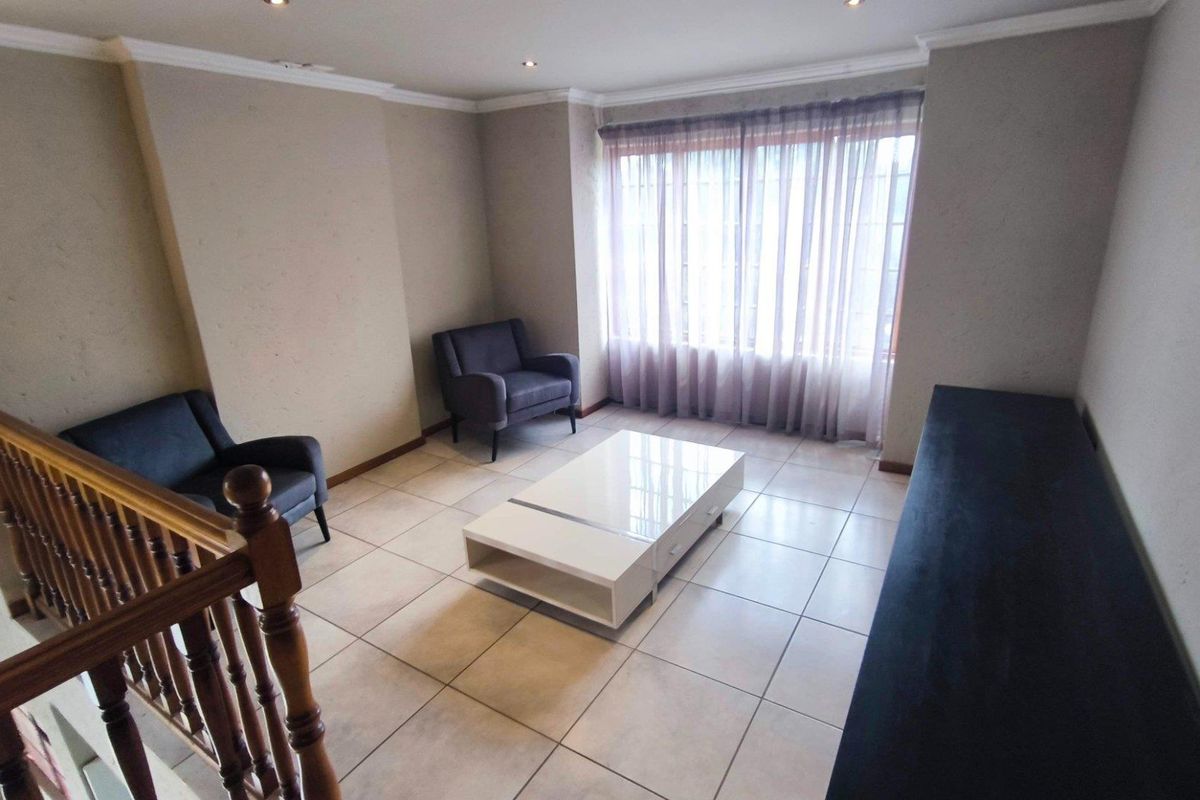 A spacious living area featuring neutral tiled flooring, recessed ceiling lighting, and a wooden staircase balustrade, offering a bright and functional space.