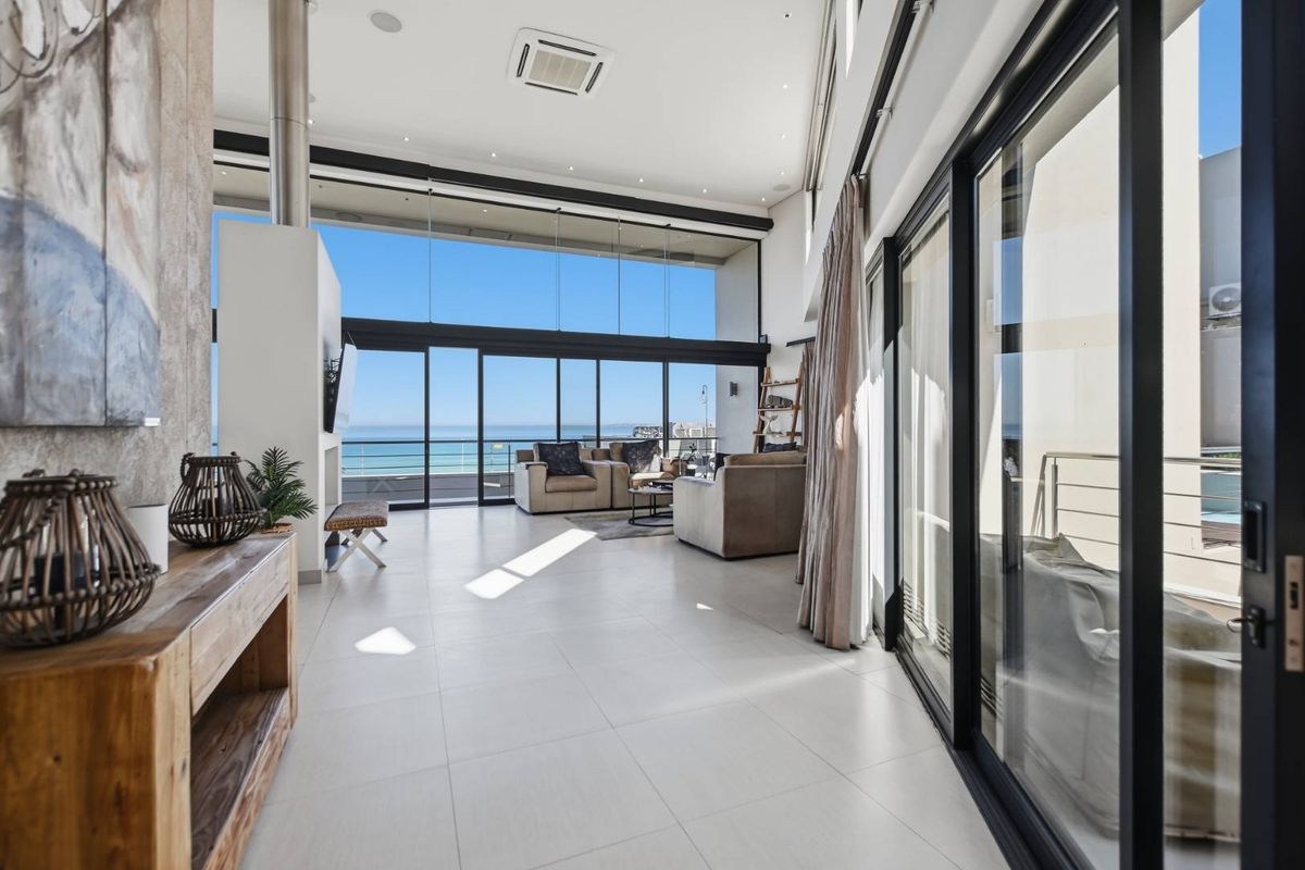 Spacious modern living area featuring high ceilings, large floor-to-ceiling glass doors with ocean views, and a sleek double-sided fireplace.