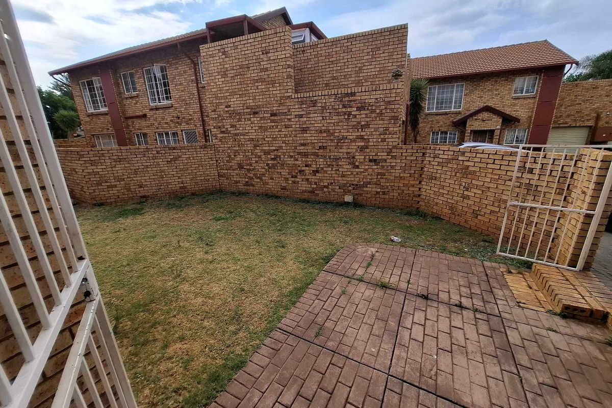 A private rear garden area featuring a paved patio, lawn, and brick boundary walls, providing a functional outdoor space for the townhouse.