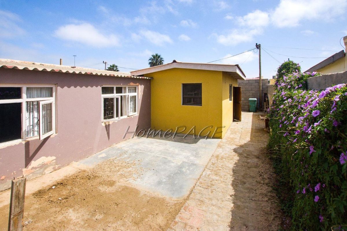A rear exterior view of the property featuring a concrete patio area, yellow and purple painted exterior walls, and a side garden path.