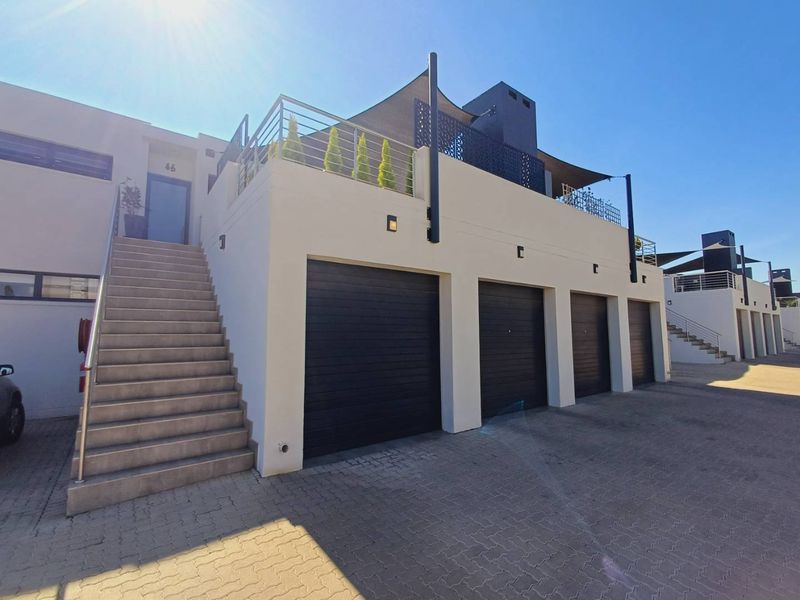 Modern townhouse exterior featuring a triple garage, paved driveway, and an elevated balcony with metal railings and shade sail.