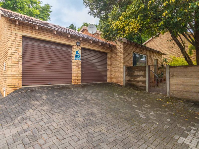 Front view of a townhouse featuring a double garage with roll-up doors, brick facade, and paved driveway.