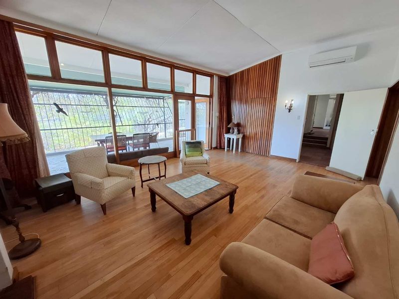 Spacious living room featuring warm hardwood flooring, distinctive timber wall paneling, and expansive windows that provide abundant natural light and access to the patio.