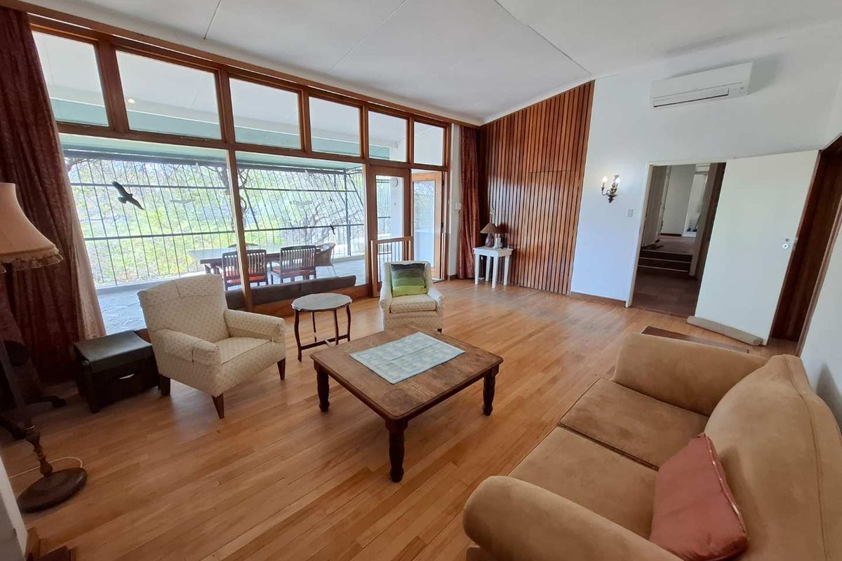 Spacious living room featuring warm hardwood flooring, distinctive timber wall paneling, and expansive windows that provide abundant natural light and access to the patio.