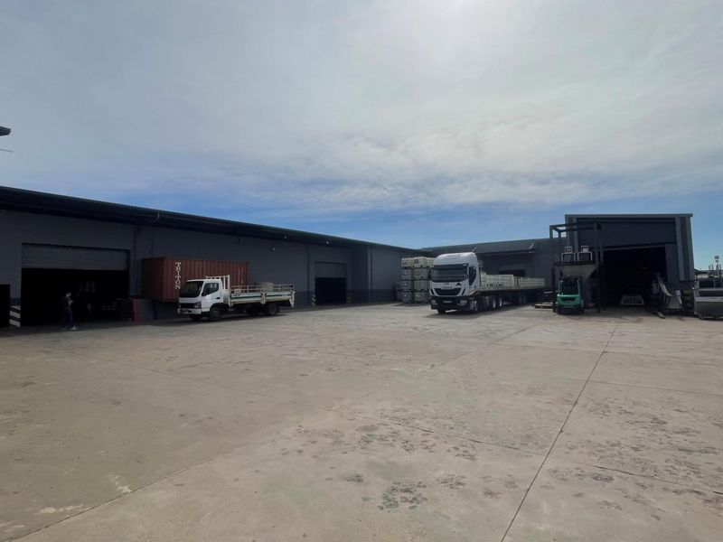 Spacious industrial yard area featuring concrete paving and multiple roller shutter access points to the warehouse facility.