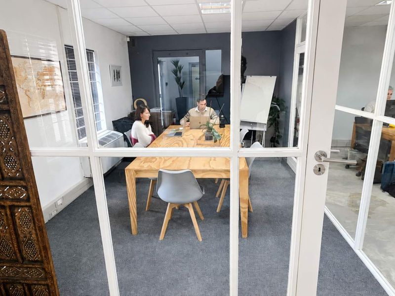 A bright office space featuring glass partition walls, carpeted flooring, and a suspended ceiling, providing a professional and collaborative work environment.