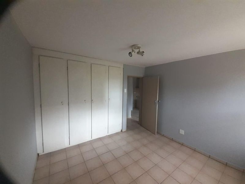 A vacant bedroom featuring built-in cupboards, tiled flooring, and neutral grey walls, offering a blank canvas for personalization.