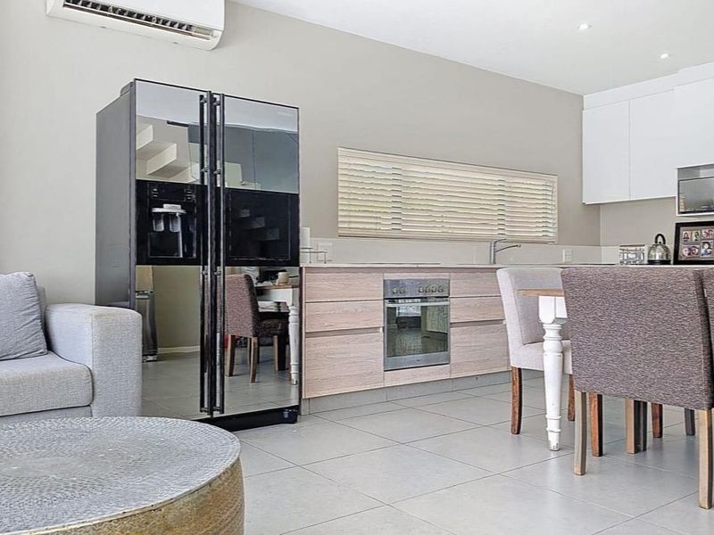Open-plan living and kitchen area featuring modern cabinetry, built-in oven, tiled flooring, and a wall-mounted air conditioning unit.