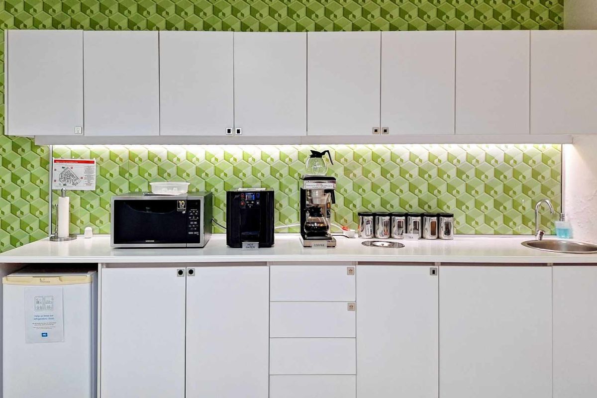 A functional office kitchenette featuring white cabinetry, a geometric green tiled backsplash, integrated sink, and ample counter space for office amenities.