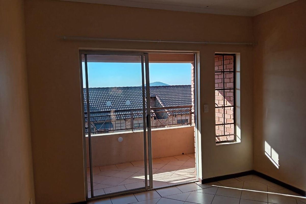A bright living area featuring tiled flooring and large sliding glass doors that open onto a private balcony with neighborhood views.