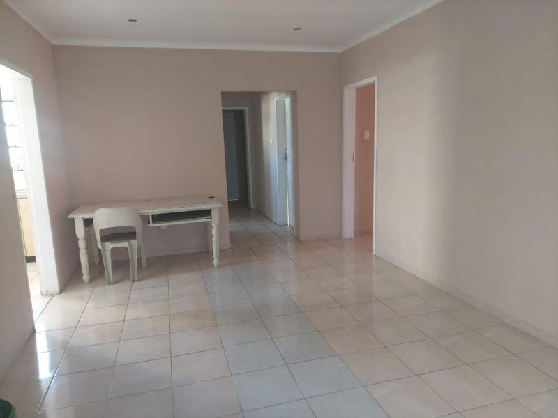 A spacious, neutral-toned living area featuring ceramic floor tiles, recessed lighting, and coved cornicing, offering a blank canvas for interior design.