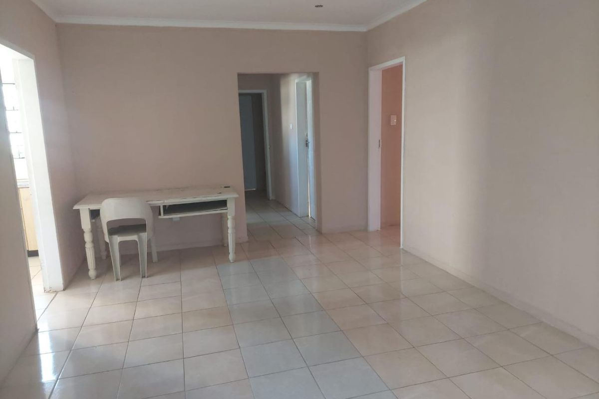 A spacious, neutral-toned living area featuring ceramic floor tiles, recessed lighting, and coved cornicing, offering a blank canvas for interior design.