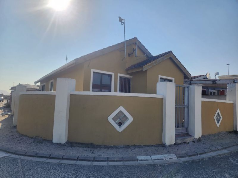 Front exterior view of a single-story house featuring a perimeter wall with decorative glass blocks, a security gate, and a tiled roof.