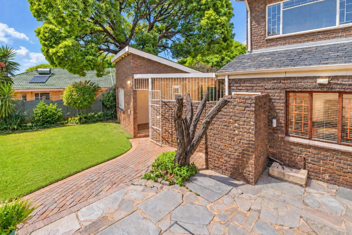 Rear exterior view featuring a brick facade, stone patio, paved walkway, and secure gated access to the property.