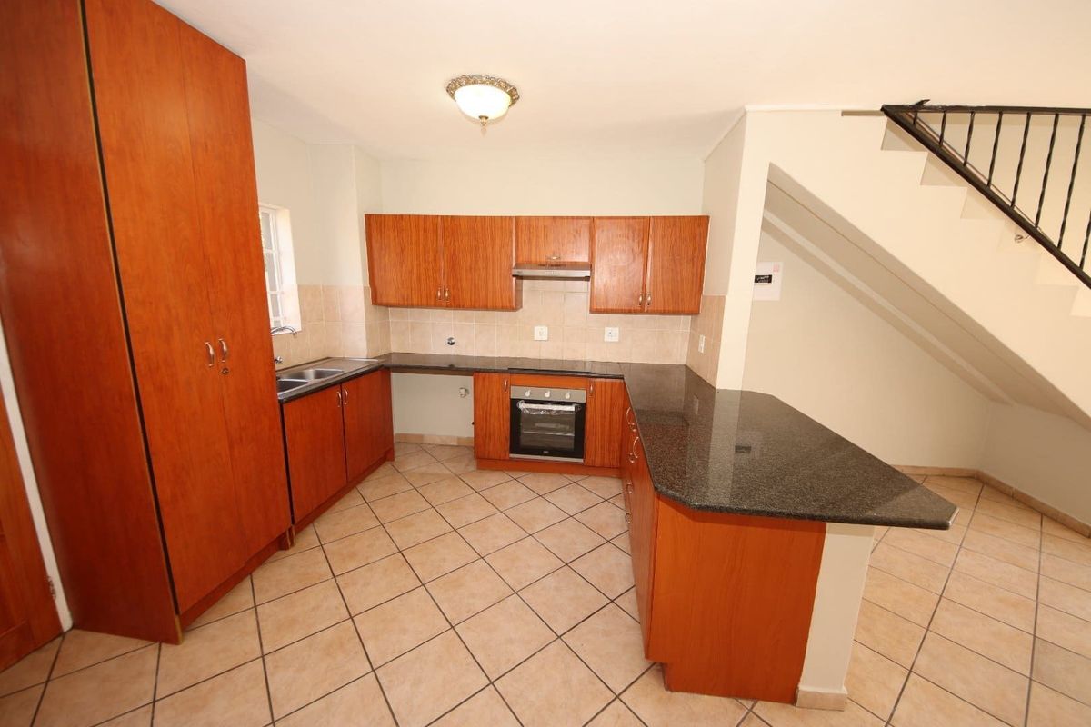 A functional kitchen featuring wooden cabinetry, granite countertops, a built-in oven, and an extractor fan, situated beneath an open staircase.