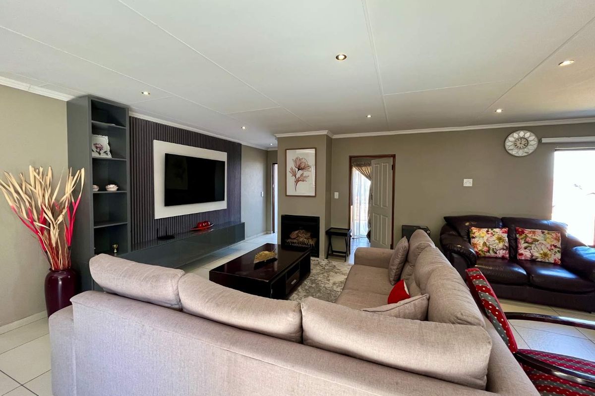 A well-maintained living room featuring a modern built-in media unit with slatted wall paneling, a fireplace, and recessed downlighting throughout.