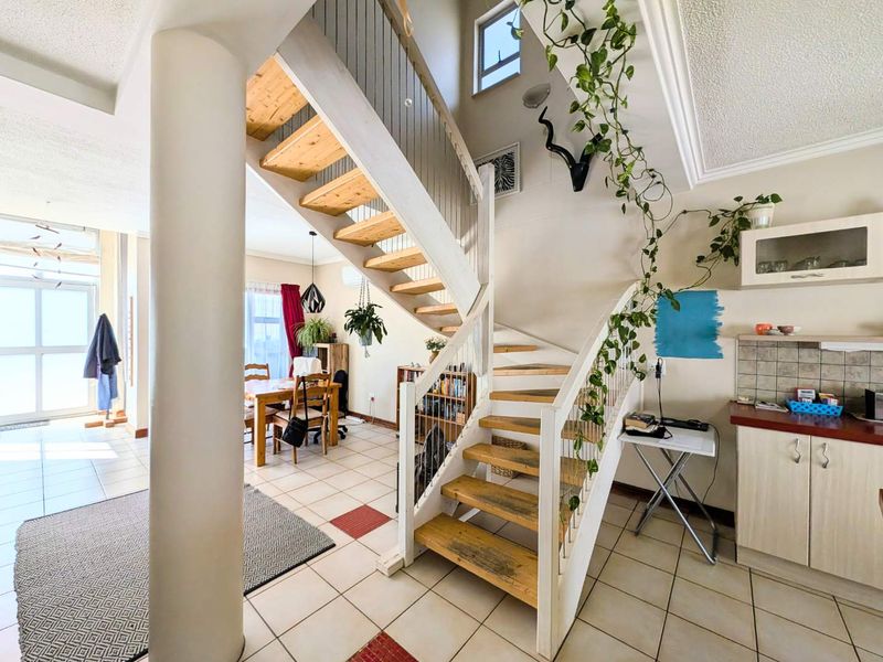 Open plan living area featuring a central staircase with wooden treads, tiled flooring, and a compact kitchen area with built-in cabinetry.