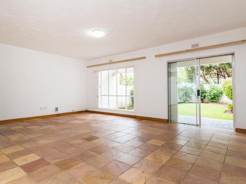 Spacious, empty living room featuring natural stone-look tiled flooring, large windows, and a sliding glass door providing direct access to the rear garden.